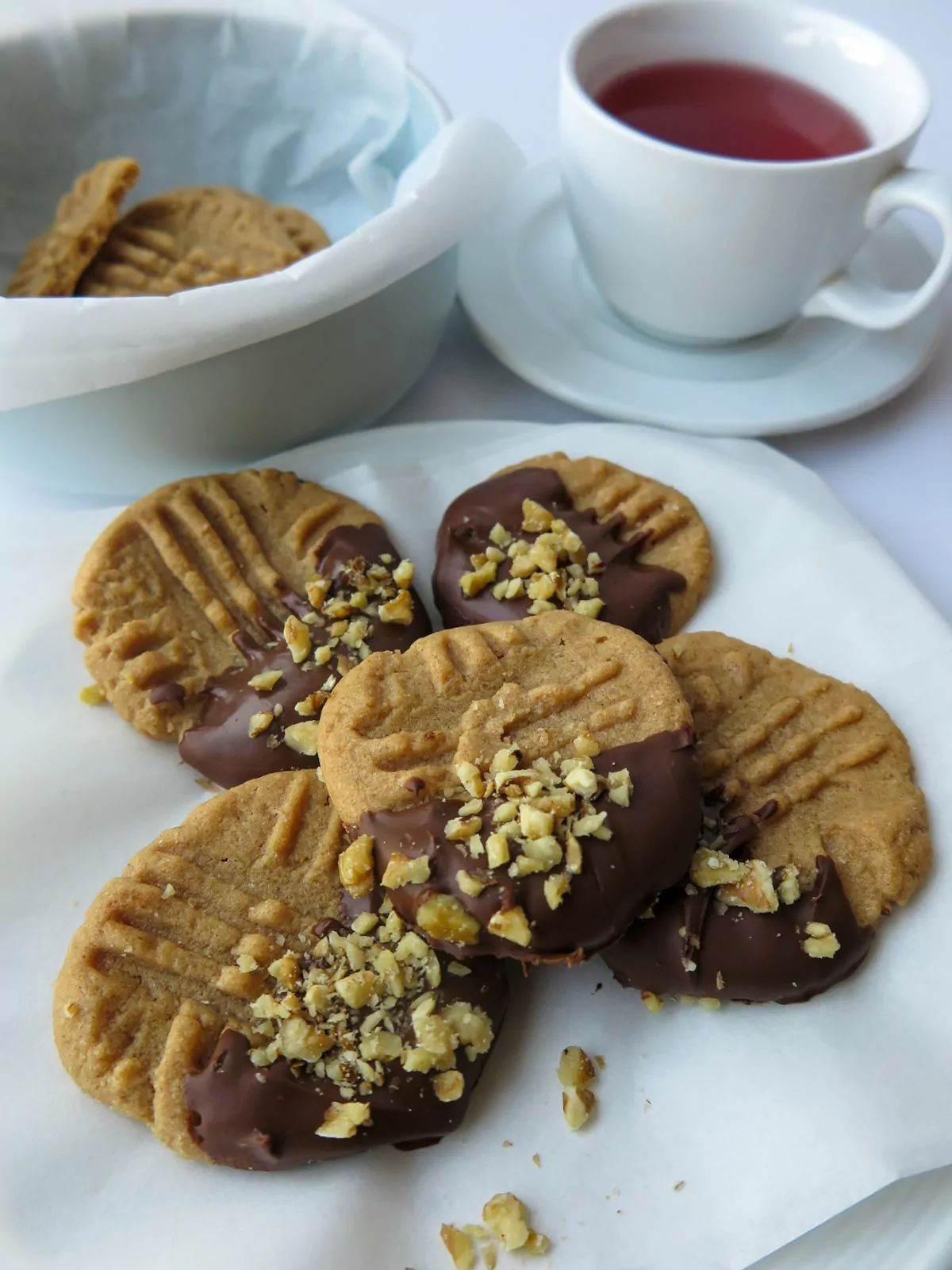 Gluten Free Peanut Butter Cookies dipped in chocolate and chopped peanuts. Tea cup in the background