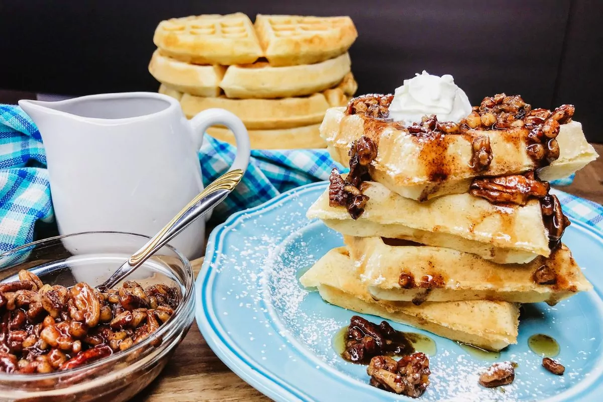 waffles stacked on blue plate with pecan topping and whipped cream.