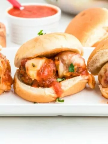 3 meatball sandwiches on a white plate.