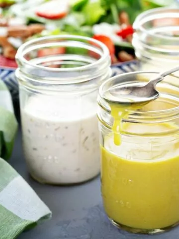 3 different salad dressings in mason jars with green plaid dish towel.