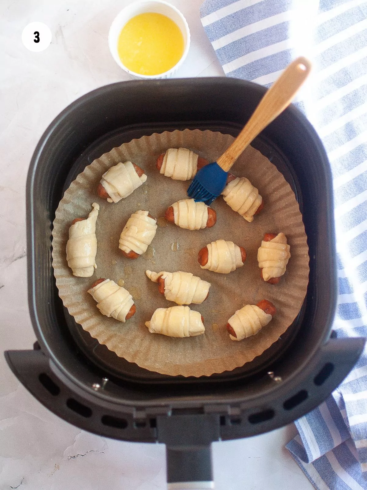 crescent wrapped sausages placed in air fryer basket brushed with butter