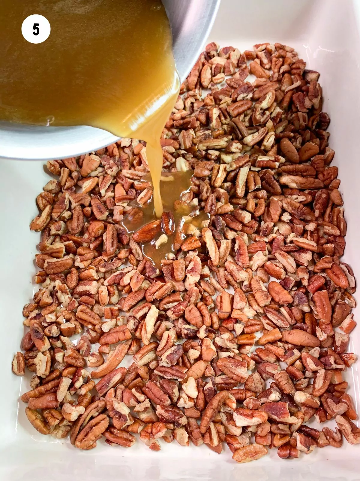 chopped pecans in the bottom of a dish with the caramel sauce being poured over them.