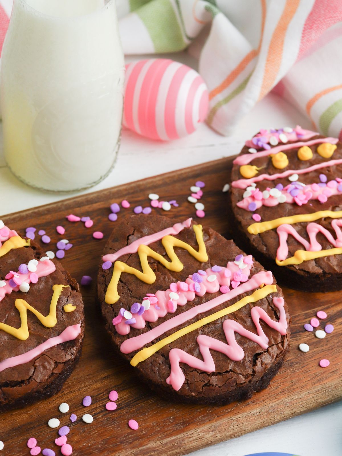 Egg shaped brownies on cutting board with glass of milk in the background.