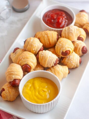 air fried sausages wrapped in crescent dough served with ramekins of ketchup and mustard