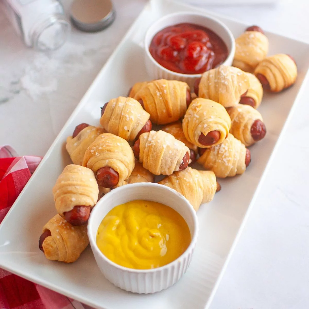 air fried sausages wrapped in crescent dough served with ramekins of ketchup and mustard