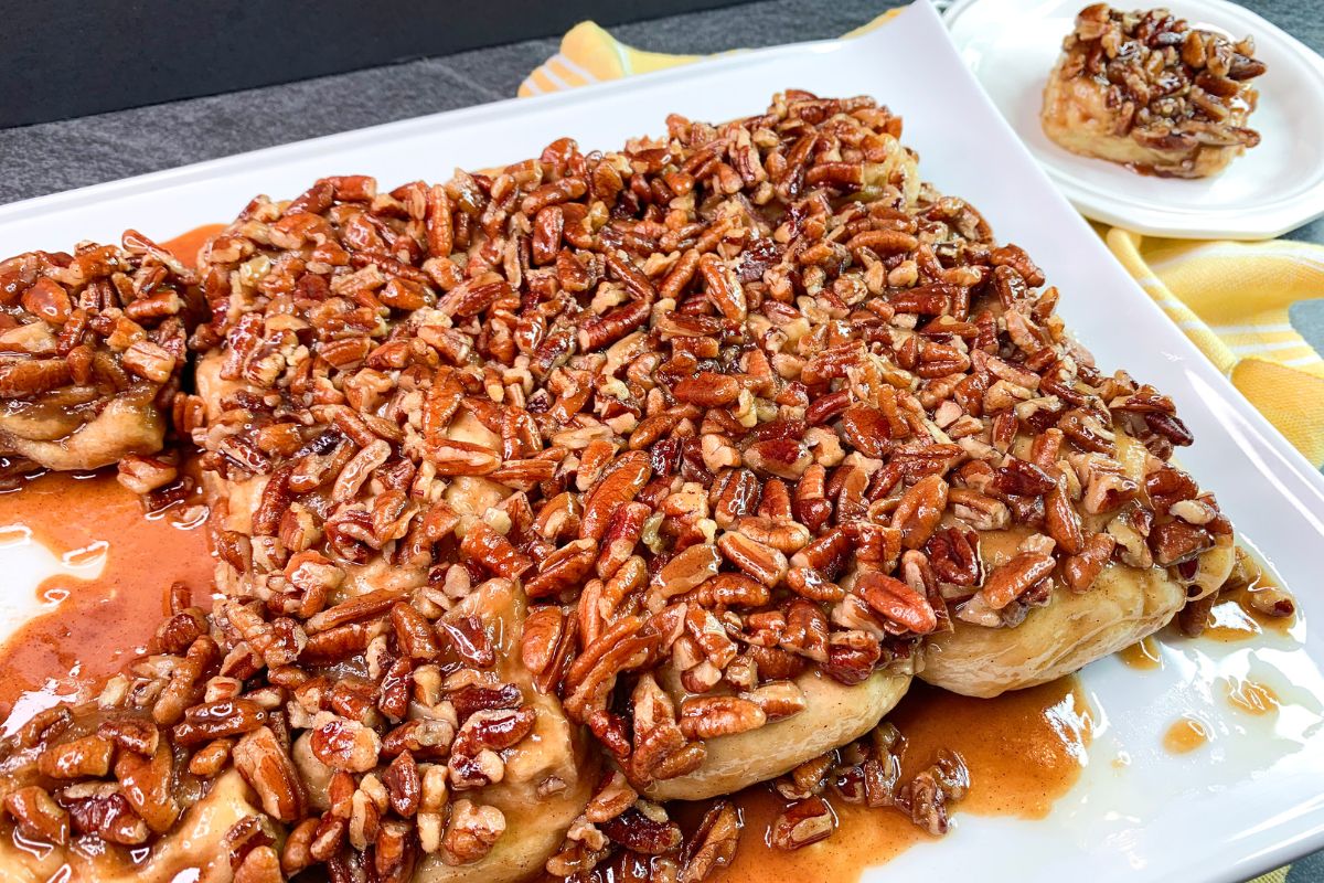 Pecan Sticky Buns on a white platter with one served on a plate.