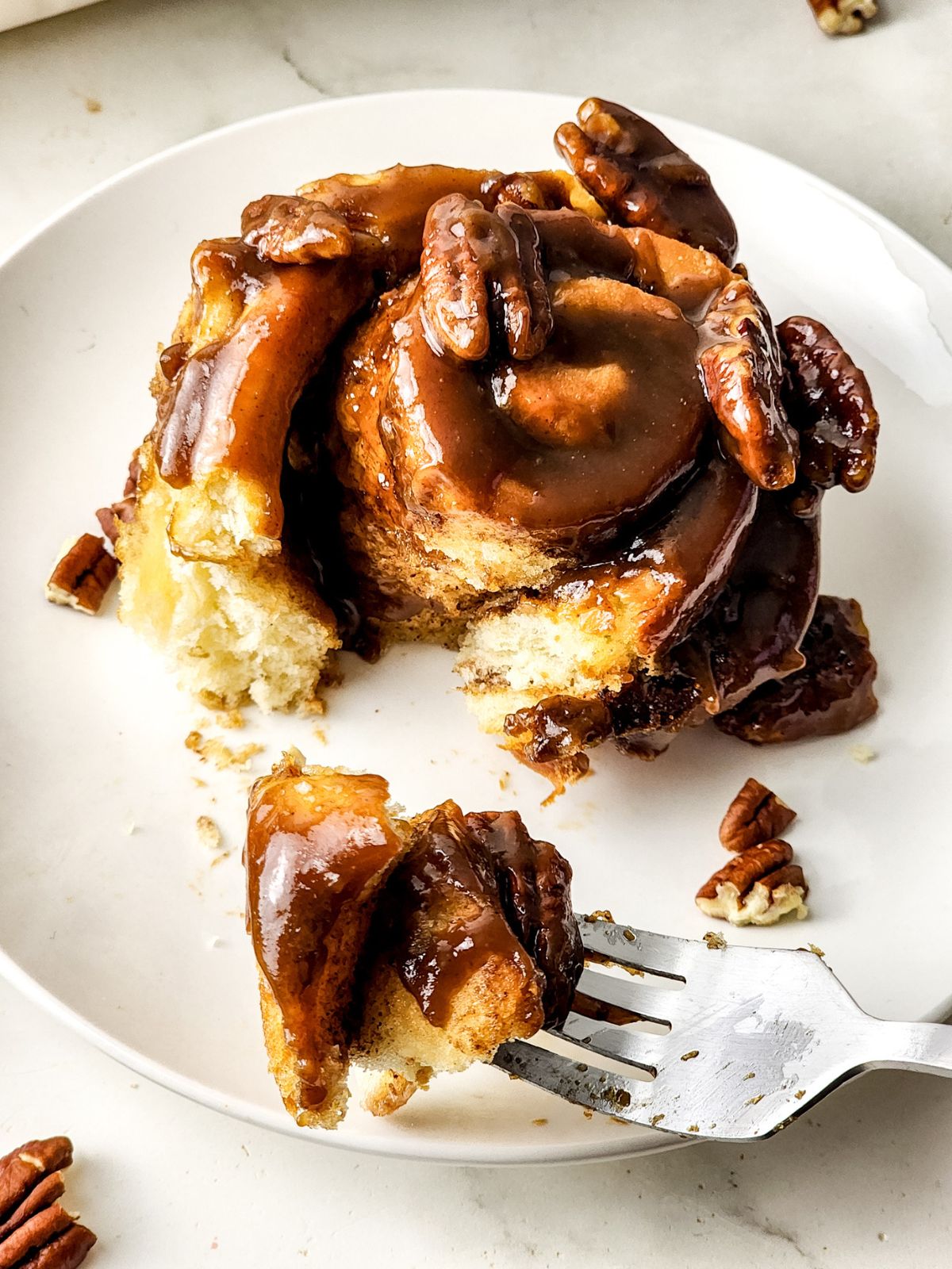 Butter Pecan sticky bun on a white plate with a piece on a fork