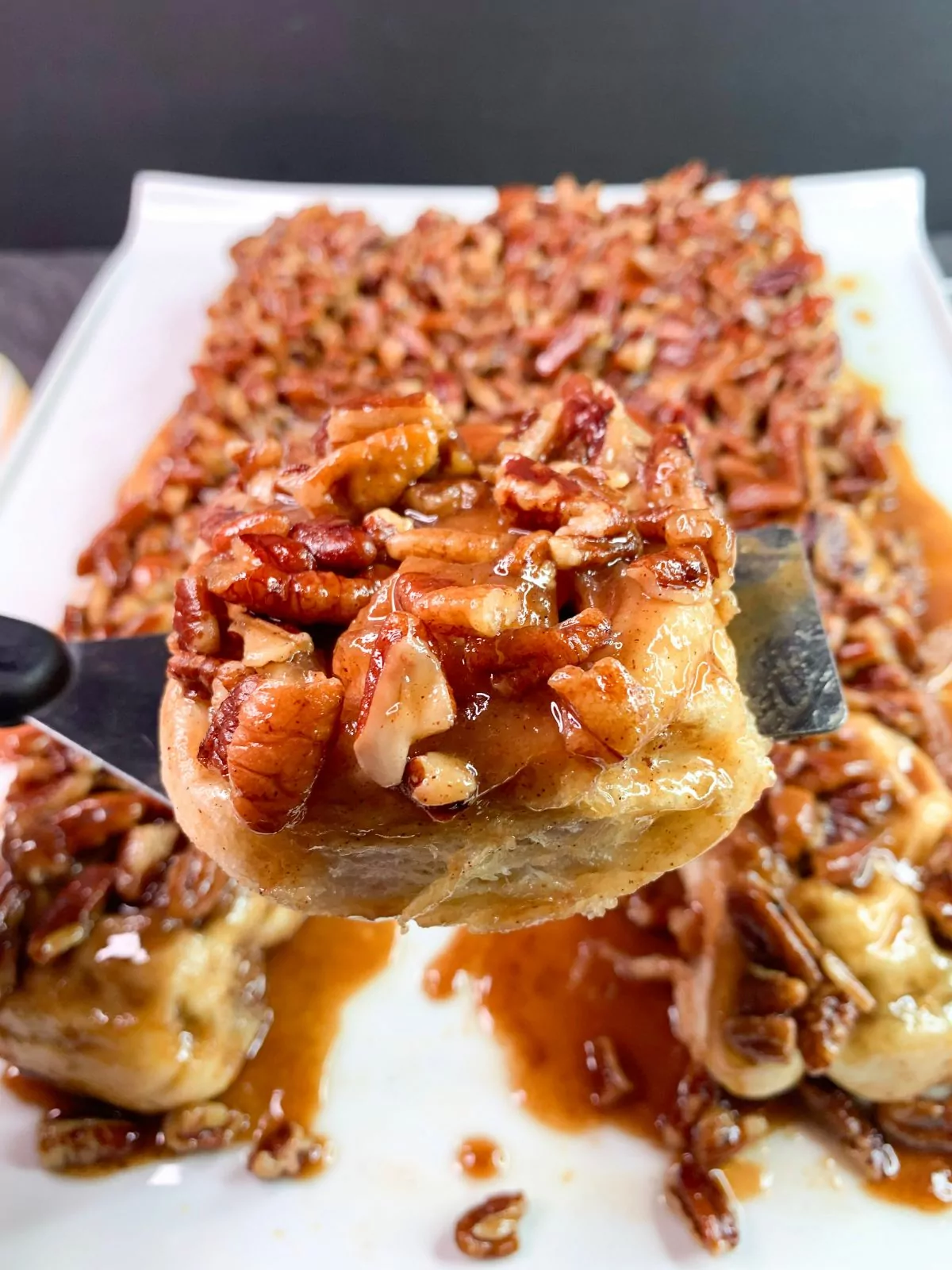 platter of pecan sticky buns with one lifted out on a spatula