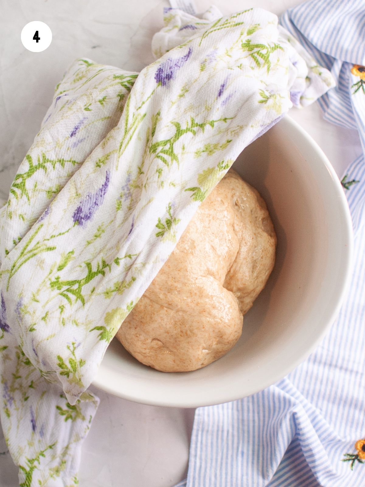 dough ball in a bowl with a towel on top to rise