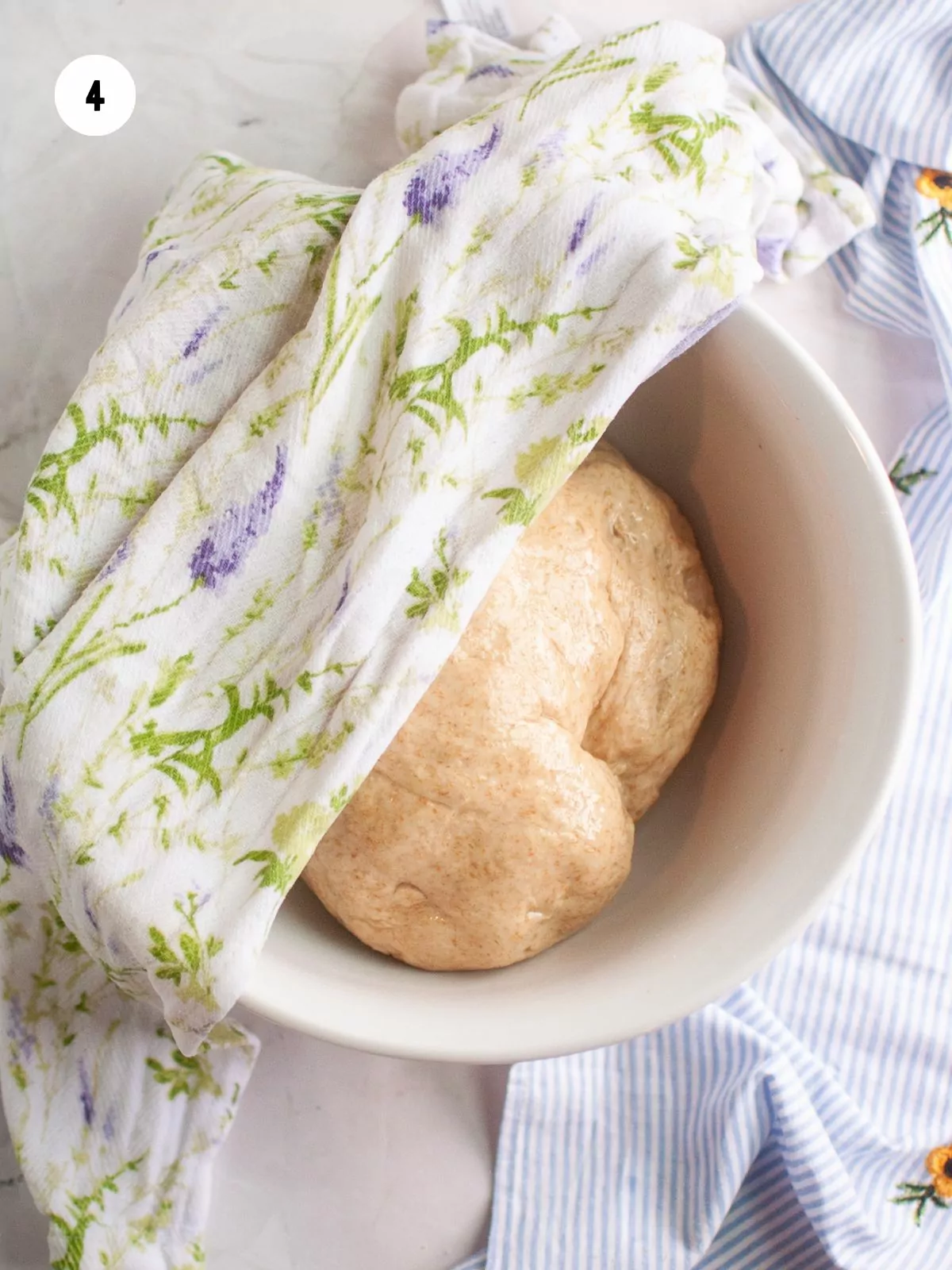 dough ball in a bowl with a towel on top to rise