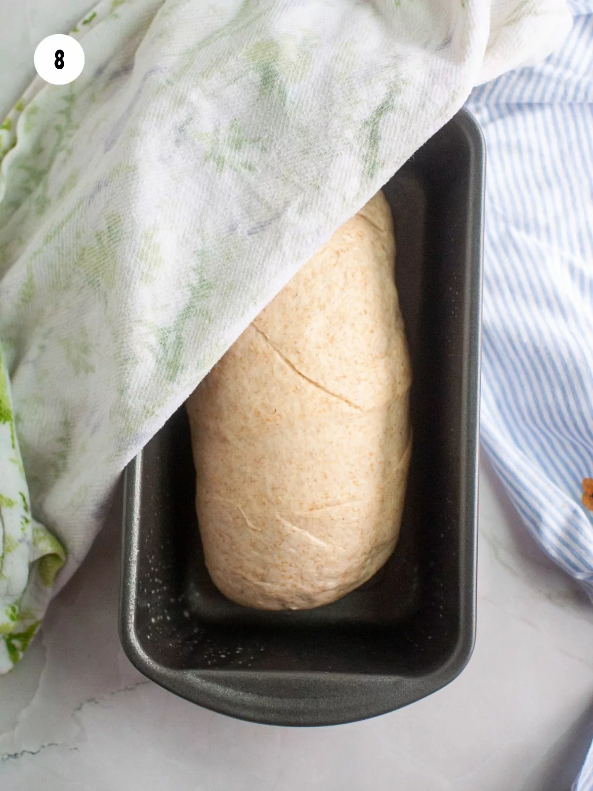 log of dough in loaf pan with a towel placed over it