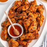 Honey Garlic Wings on a white serving platter with a ramekin of honey and honey dipper