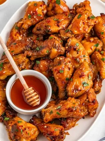Honey Garlic Wings on a white serving platter with a ramekin of honey and honey dipper