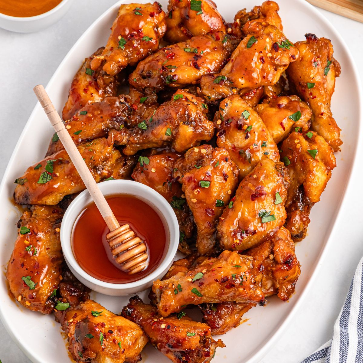 Honey Garlic Wings on a white serving platter with a ramekin of honey and honey dipper