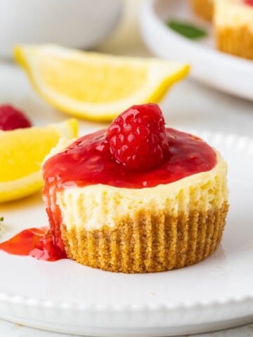 Mini Cheesecakes topped with raspberry sauce. Lemon slices in the background