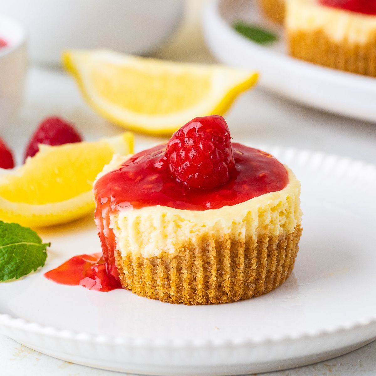 Mini Cheesecakes topped with raspberry sauce. Lemon slices in the background