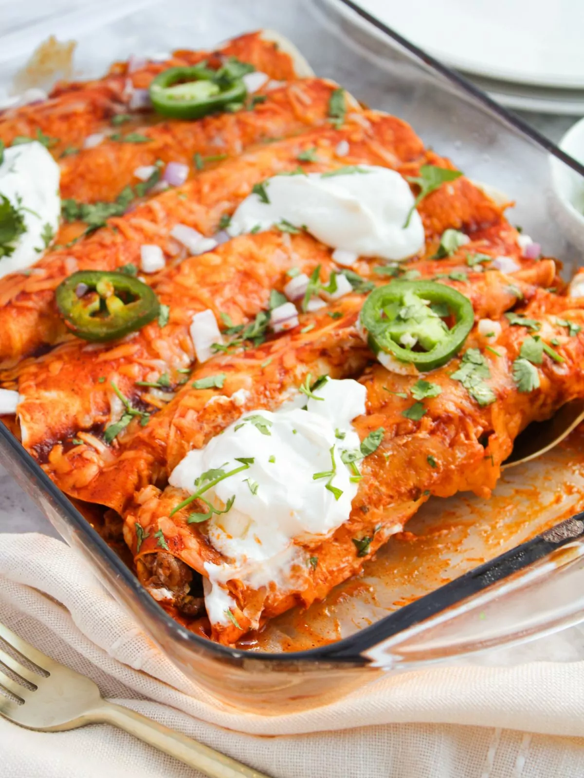 glass baking dish filled with beef enchiladas with sour cream and jalapeno on top