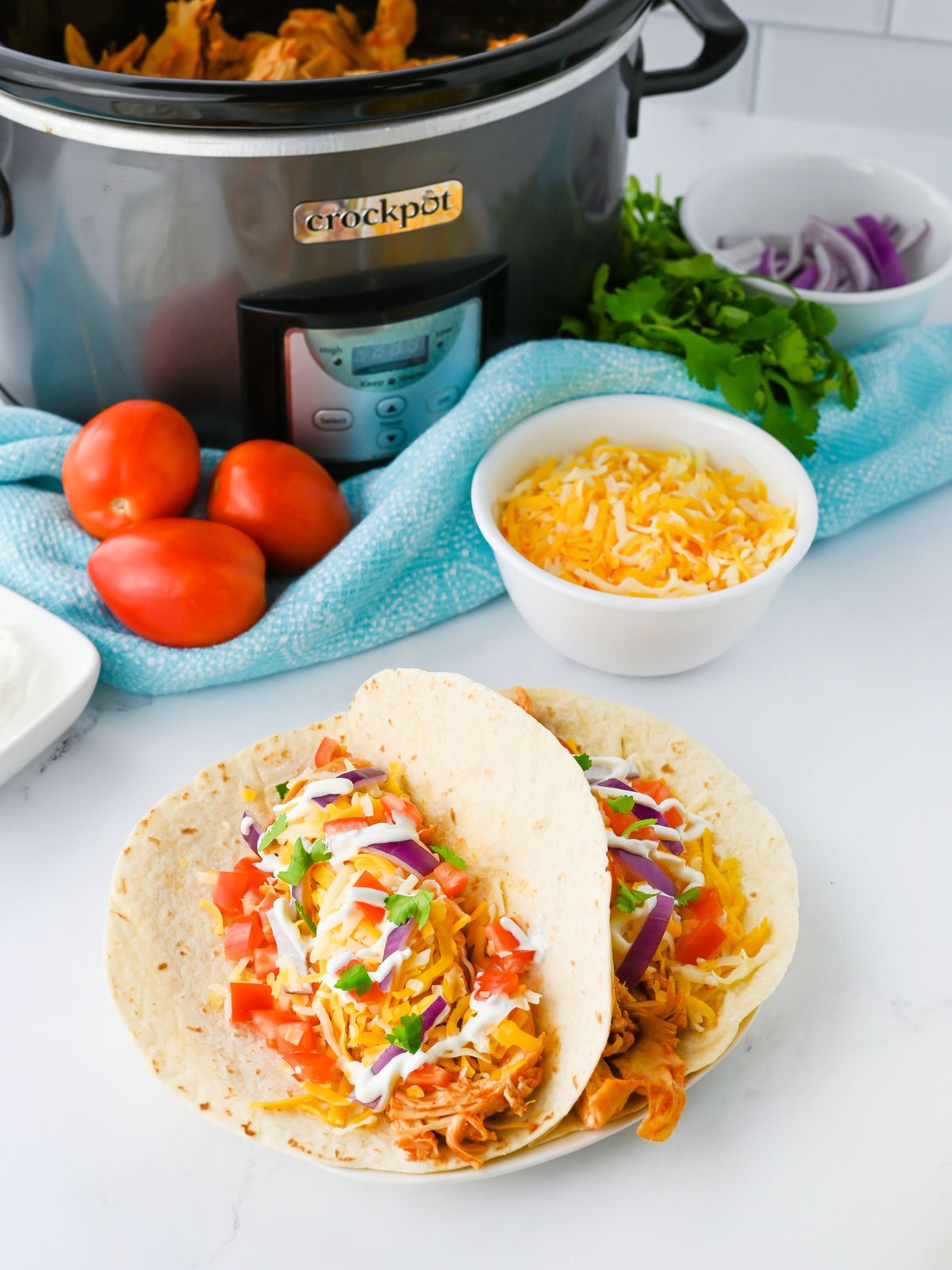 Shredded Chicken Tacos with a Crockpot filled with shredded chicken and taco toppings in the background