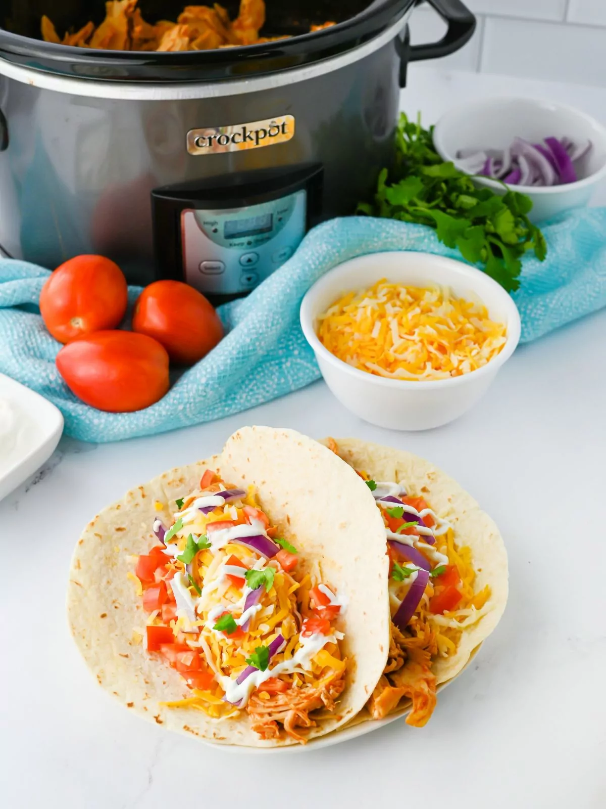 Shredded Chicken Tacos with a Crockpot filled with shredded chicken and taco toppings in the background