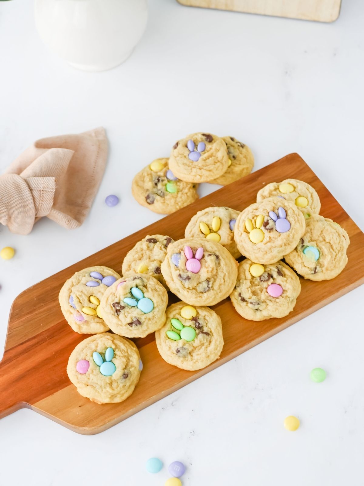 wooden board filled with chocolate chip cookies and pastel M&M's that make bunnies with a pink towel in the background