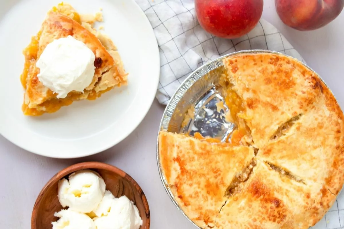 slice of peach pie on plate with full pie in pie plate. Bowl of ice cream to the side MSN.