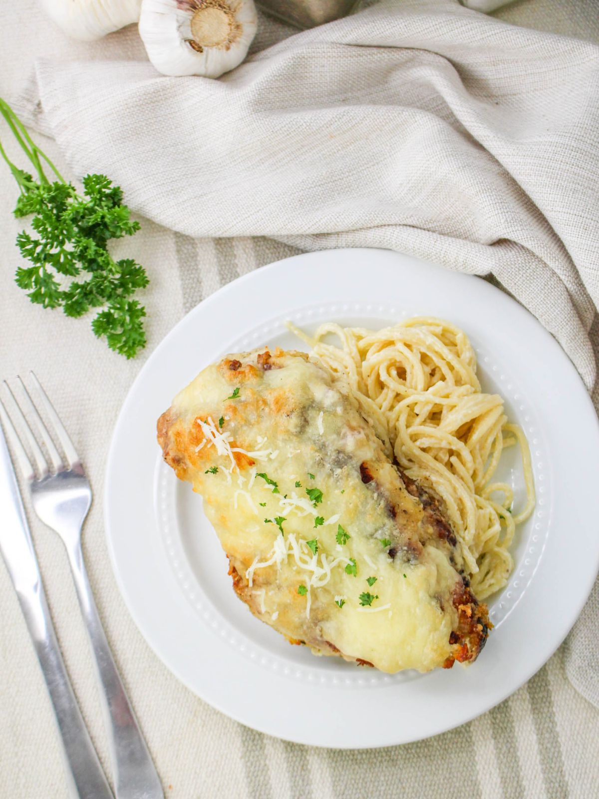 plate of Baked Chicken Cutlet Alfredo served with pasta on a striped tablecloth