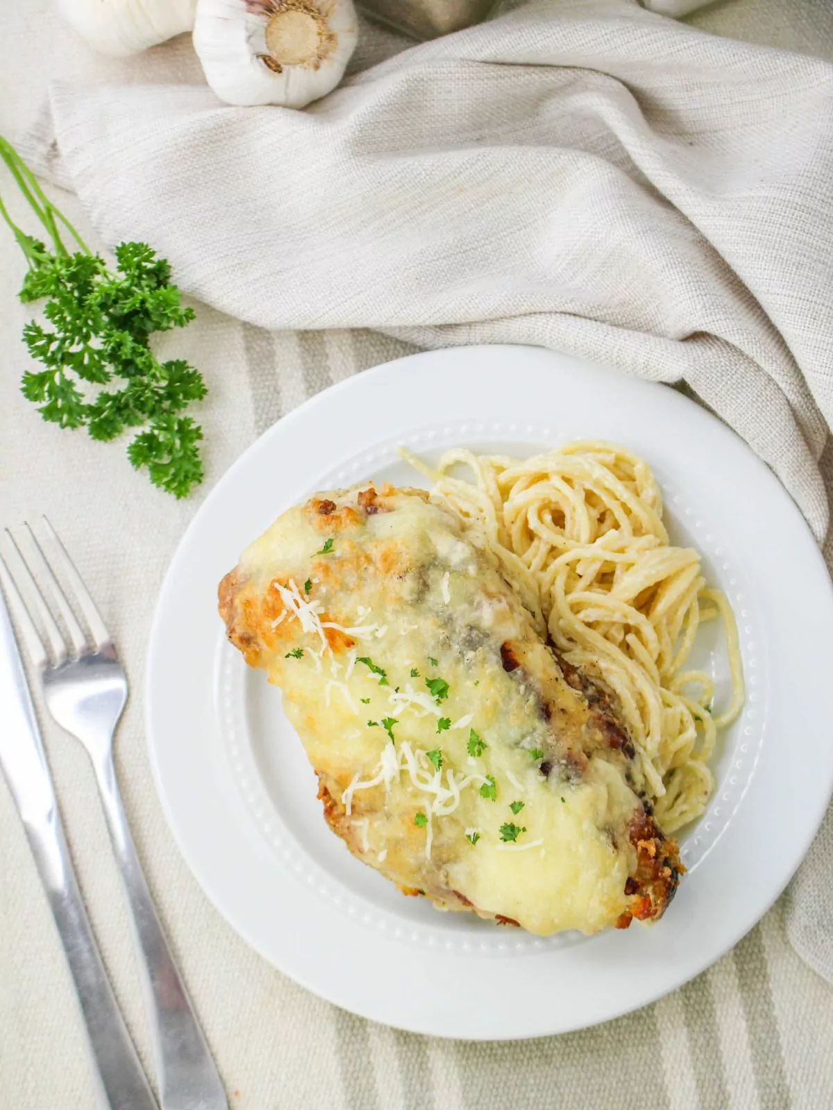 plate of Baked Chicken Cutlet Alfredo served with pasta on a striped tablecloth
