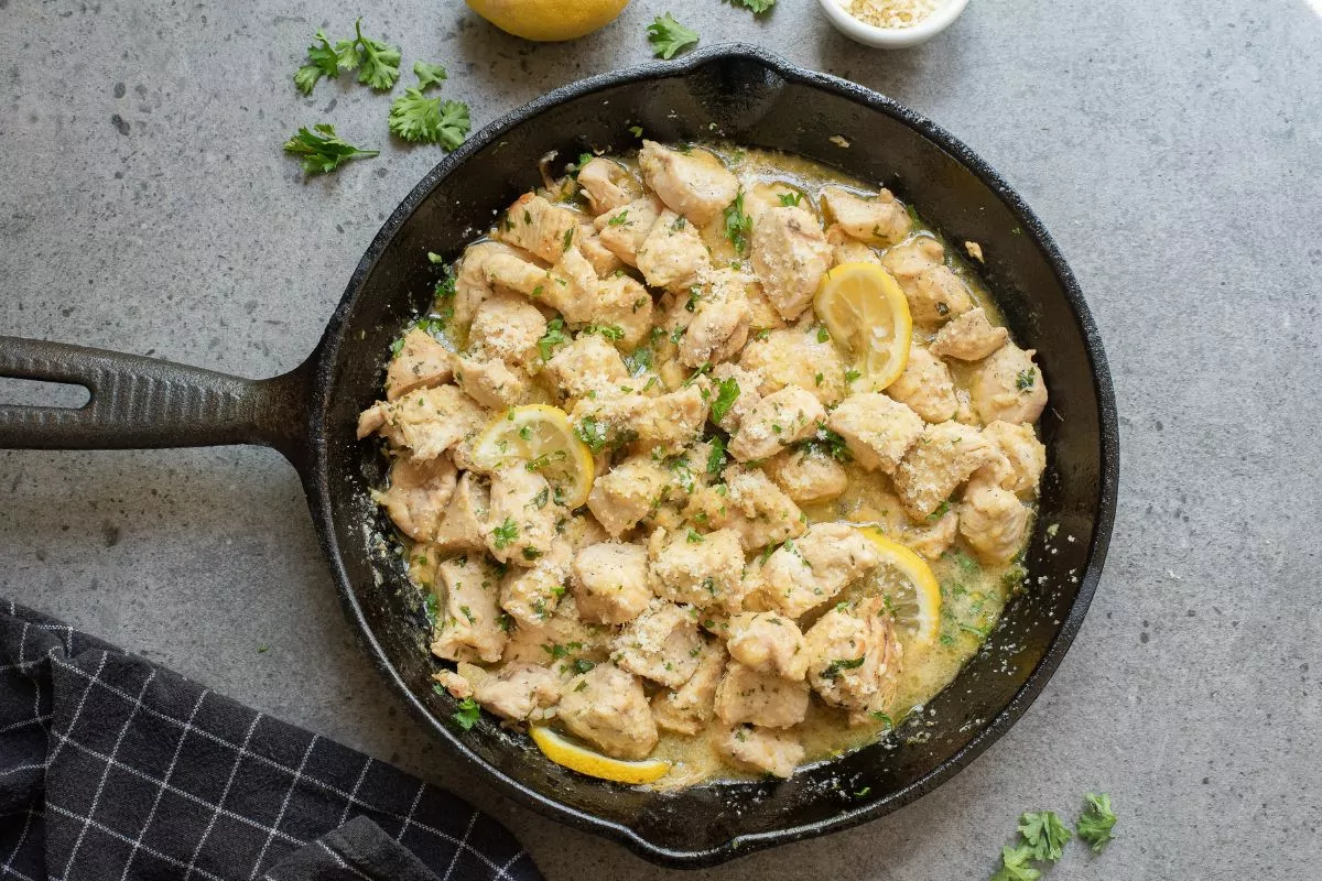 Garlic Chicken Bites topped with lemon slices and parmesan cheese in a cast iron pan