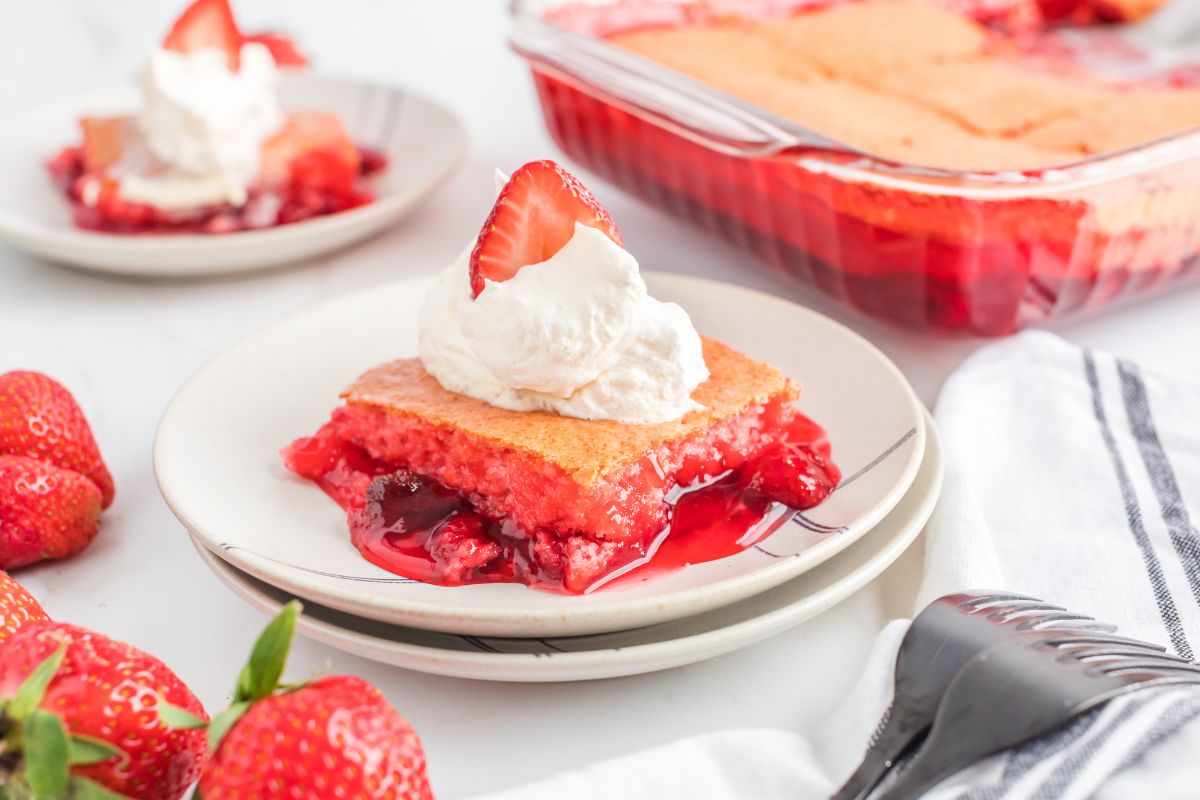 Strawberry Dump Cake on a plate with whipped topping and the rest of the cake in the background