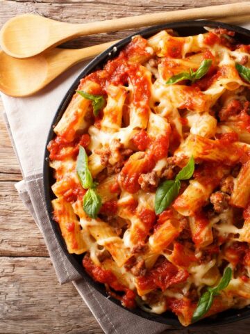pasta with cheese and fresh basil leaves on black plate.