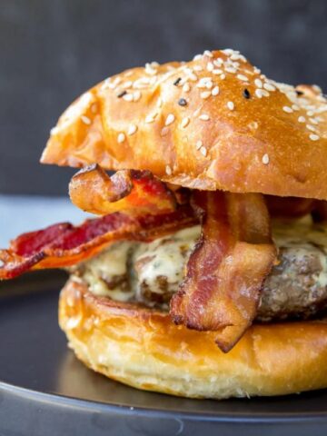 bacon burger with cheese on black plate.