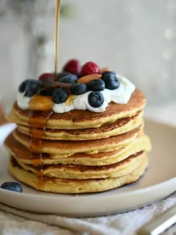 stack of pancakes with blueberries, whipped cream and syrup.