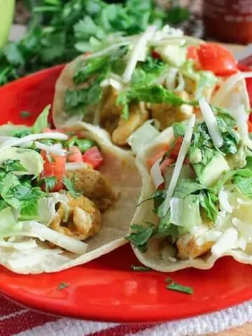 chicken tacos in soft shells on red plate.