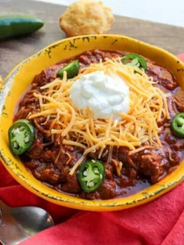bowl of chili with jalapenos and corn muffins.