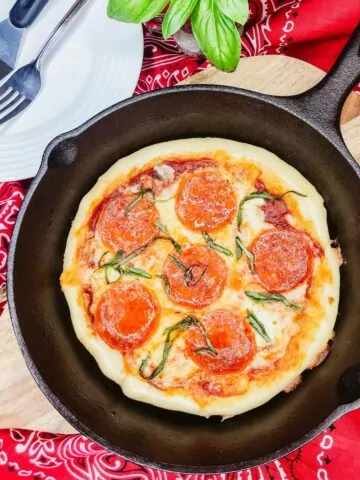 pepperoni pizza made in a cast iron pan on cutting board.