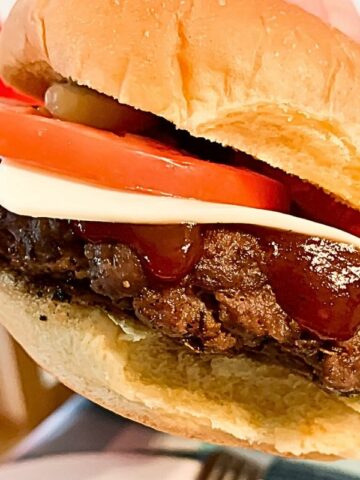 burger held in hands with ketchup, tomato, cheese and pickles.