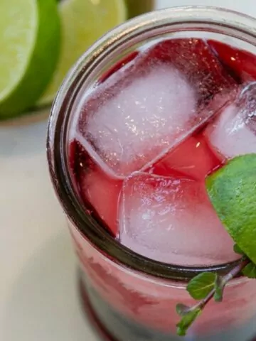 cherry mocktail in glass with ice cubes, lime wedge and fresh mint leaves.