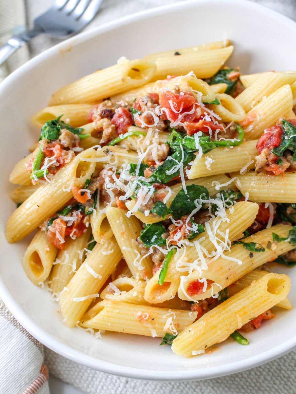 Creamy Sausage Pasta with Spinach served in a shallow white bowl