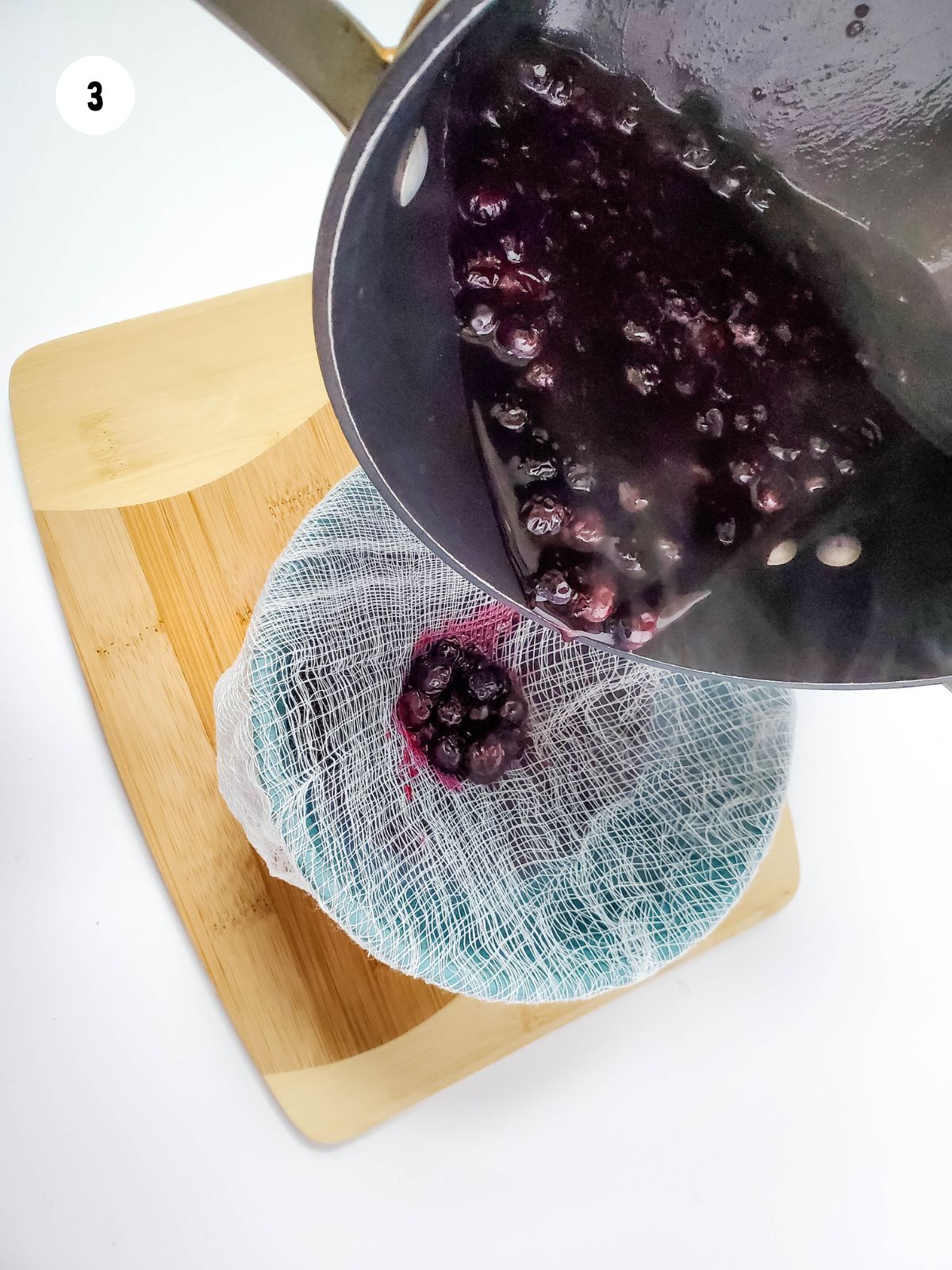 blueberry syrup being strained through cheesecloth