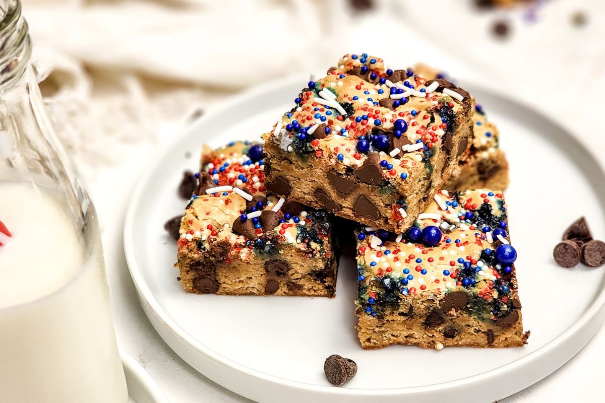 Chocolate chip cookie bars with patriotic sprinkles stacked on a white plate.