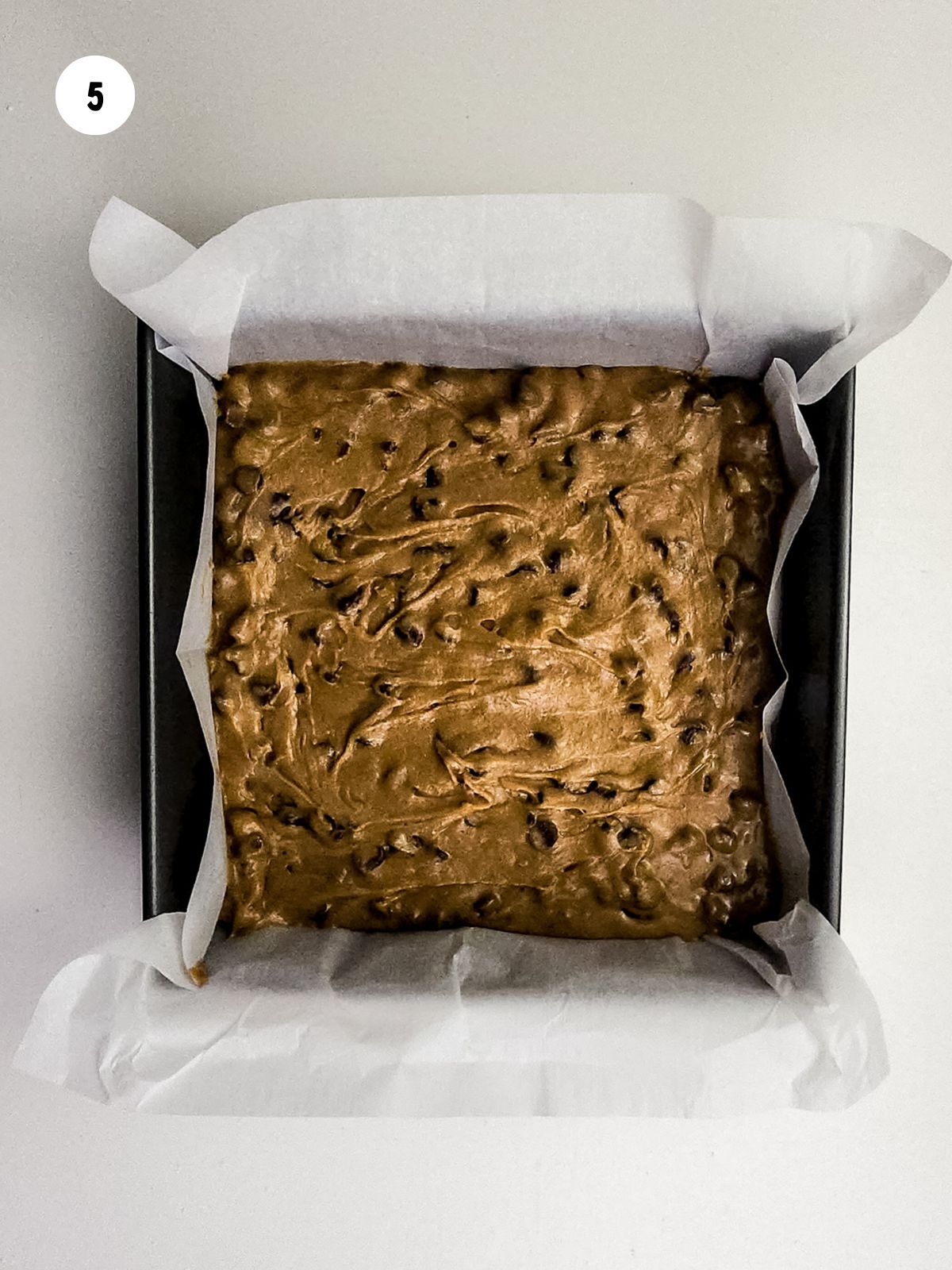 Cookie batter spread evenly in a square baking pan lined with parchment paper.