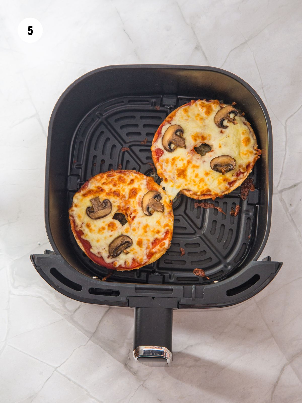 Air fried pizza bagels in the air fryer basket.