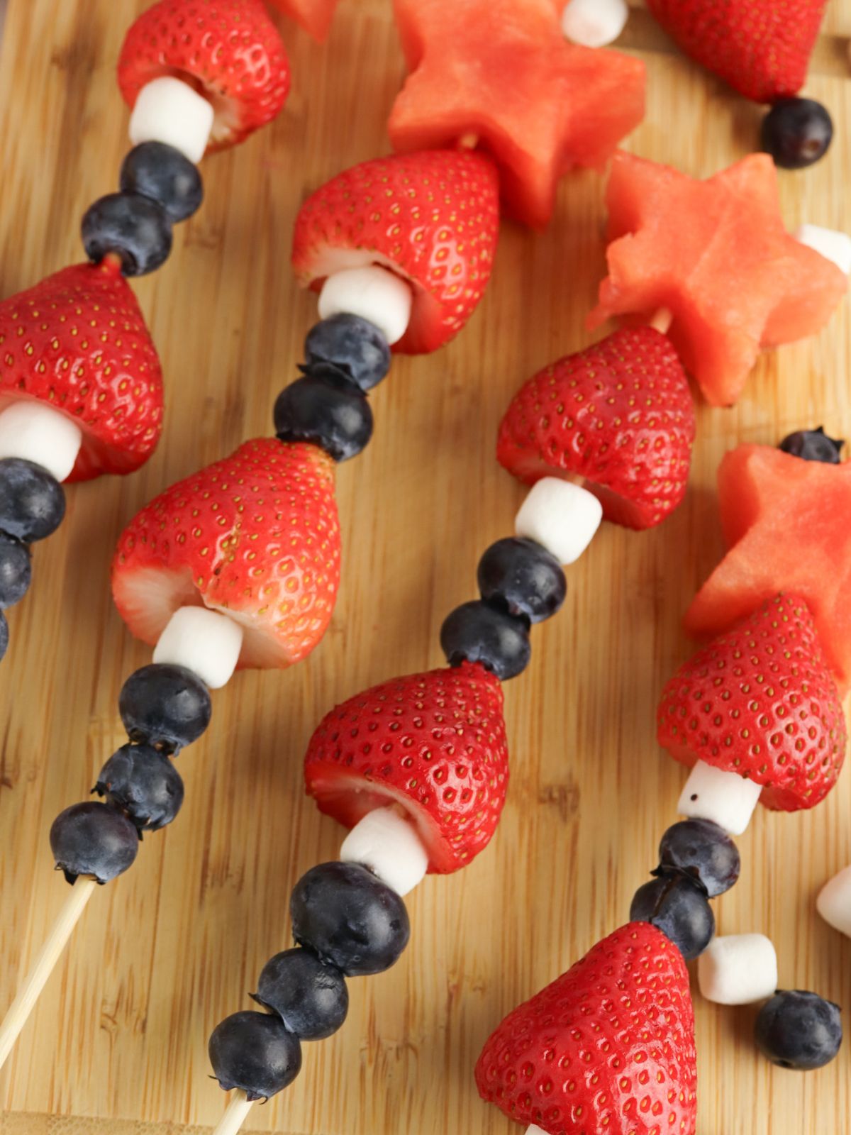 Red white and blue fruit kabobs on a wood cutting board.