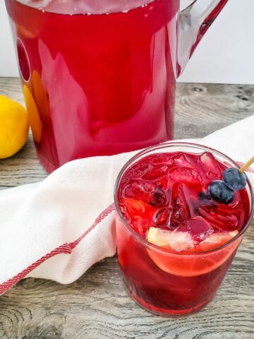 Blueberry Lemonade served in a glass with a wedge of lemon and a skewer of blueberries