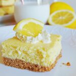 lemon cheesecake bar topped with whipped cream and lemon wedge