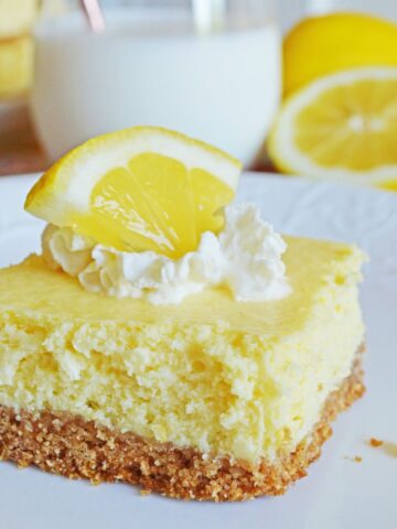 lemon cheesecake bar topped with whipped cream and lemon wedge