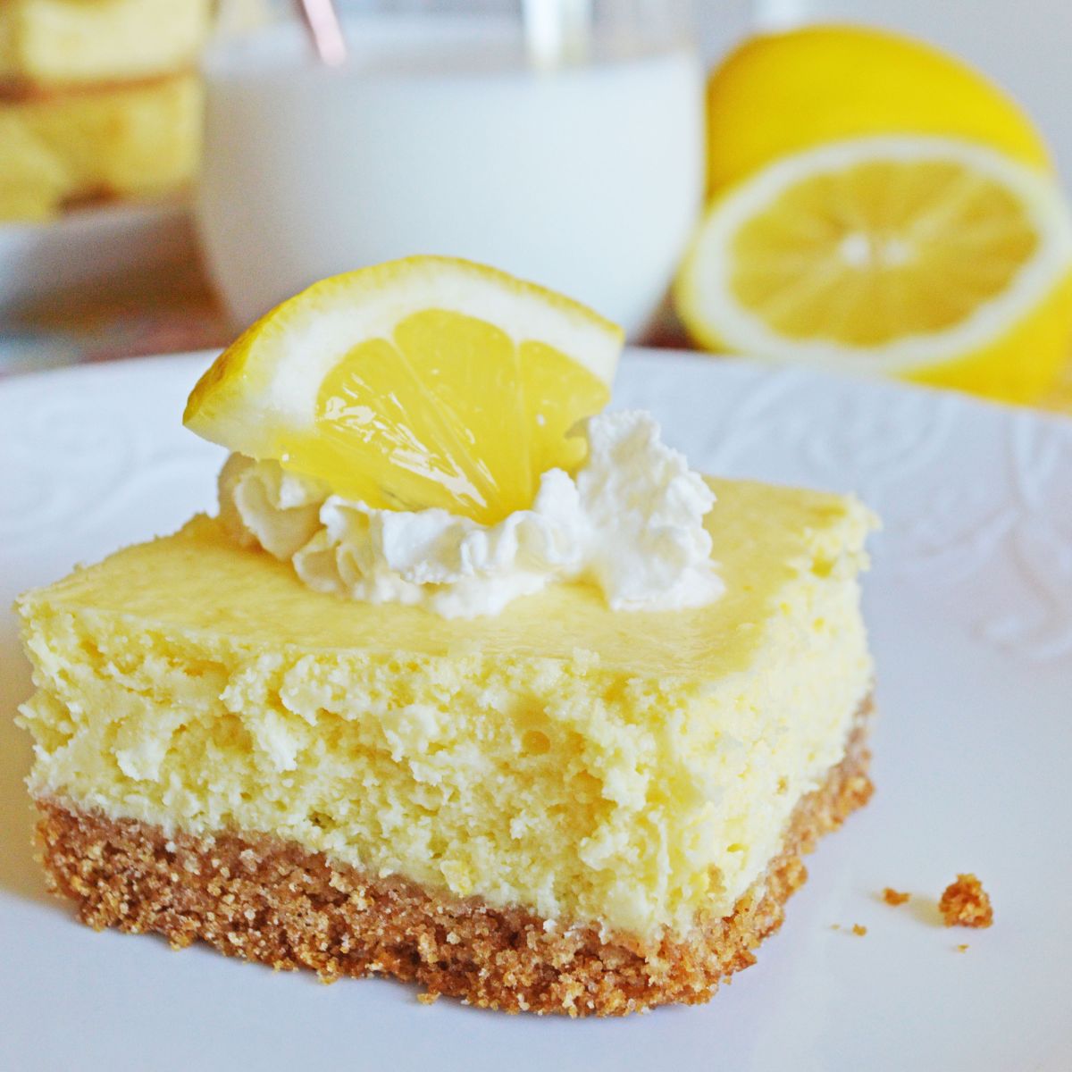 lemon cheesecake bar topped with whipped cream and lemon wedge
