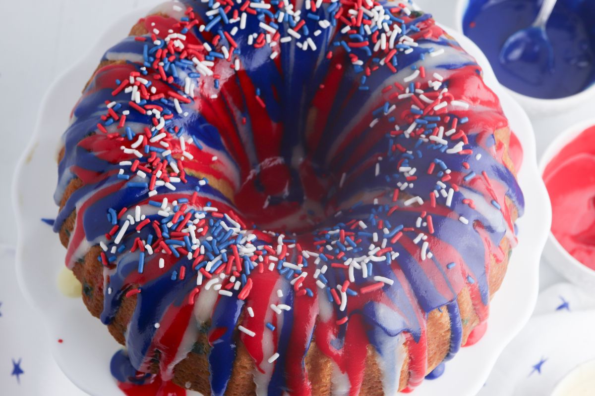 Overhead view of a pound cake with red white and blue icing drizzled on top with patriotic sprinkles.
