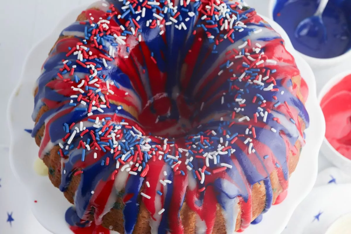 Overhead view of a pound cake with red white and blue icing drizzled on top with patriotic sprinkles.