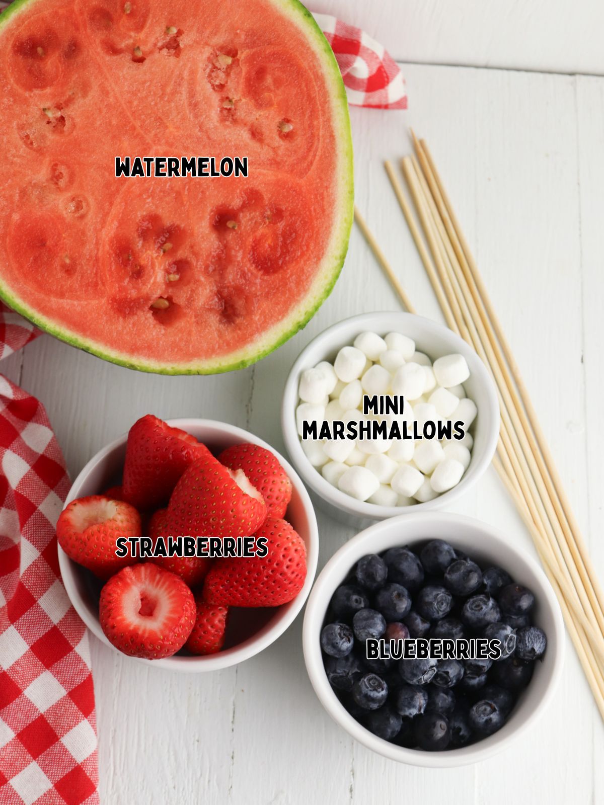 watermelon, bowl of strawberries with the tops cut off, a bowl of mini marshmallows, and a bowl of blueberries.